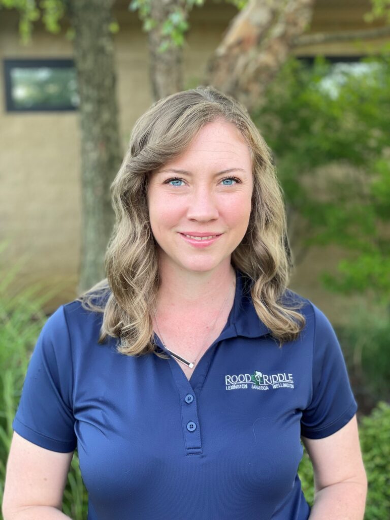 A woman in blue shirt standing next to tree.