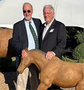 Two men standing next to a horse statue.