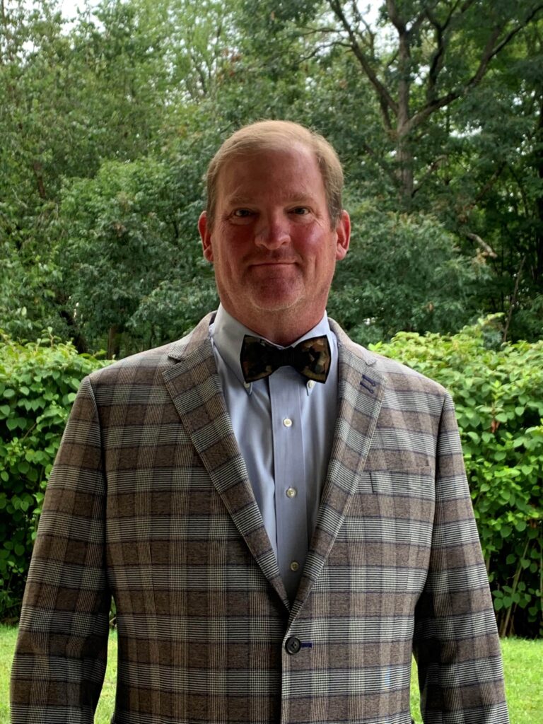 A man in a suit and bow tie standing outside.