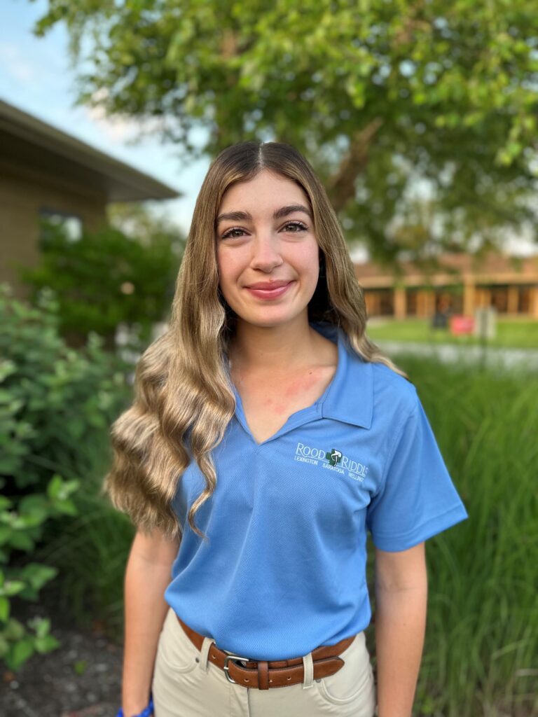 A woman in blue shirt standing next to grass.